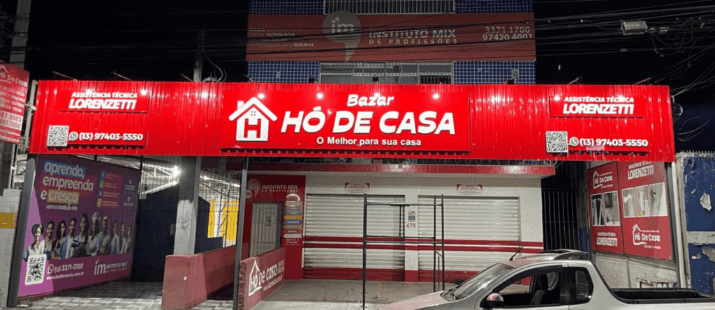 Fachada em ACM na cor vermelha com letras com PVC Expandido na cor branca, iluminada por refletores. A empresa fica localizada na cidade de São Vicente-SP.